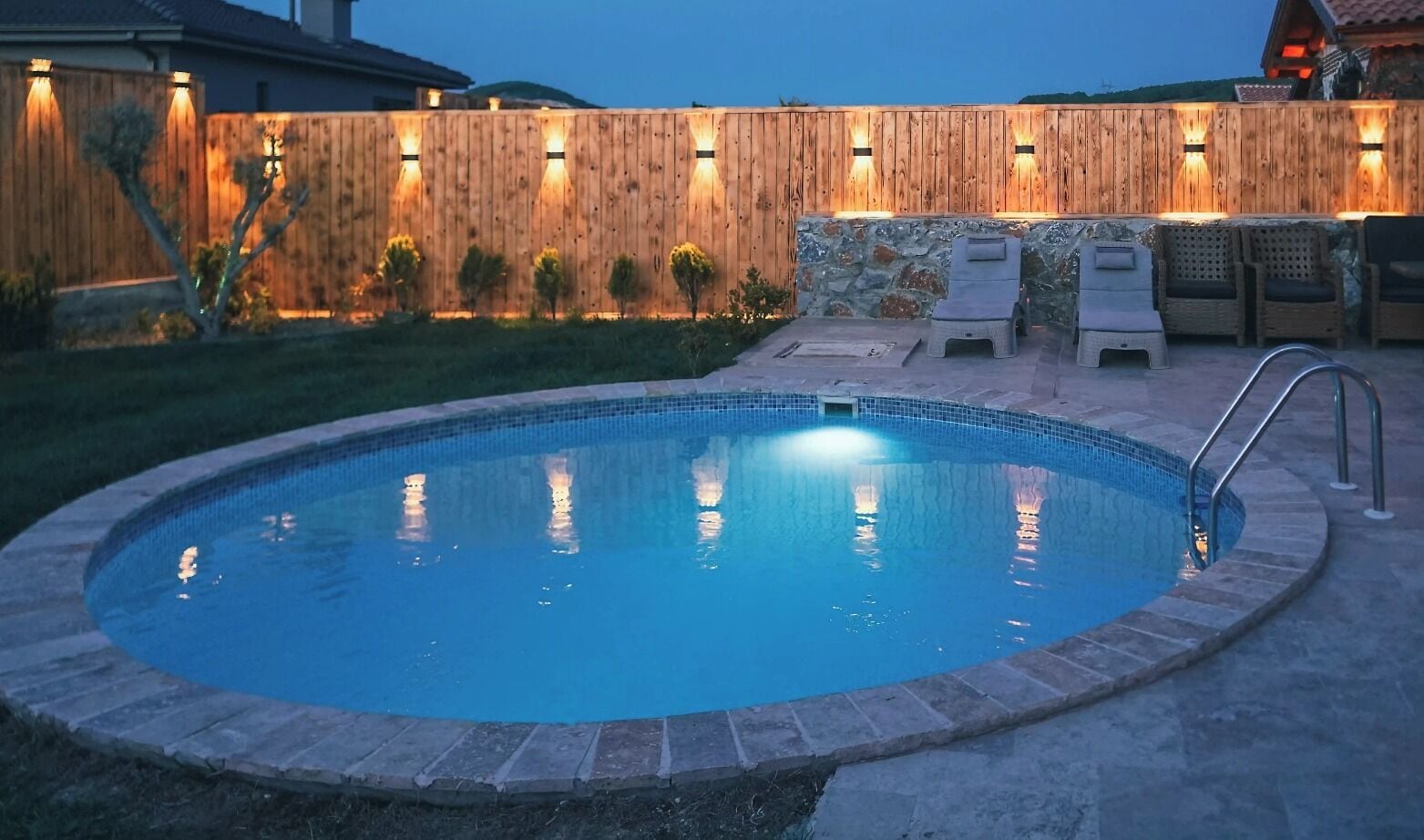 Piscina com cerca de madeira, parede de pedra e área de estar ao ar livre.