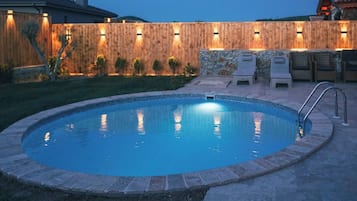 Piscina com cerca de madeira, parede de pedra e área de estar ao ar livre.