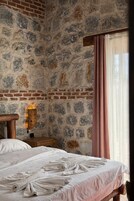 Un dormitorio con pared de piedra, cabecero de madera, mesita de noche con lámpara y ventana con cortinas.