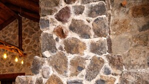 Une cheminée en pierre avec un feu, un canapé beige et un mur en pierre.