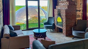 Un intérieur rustique avec des murs en pierre, une cheminée et une grande fenêtre donnant sur un paysage verdoyant.