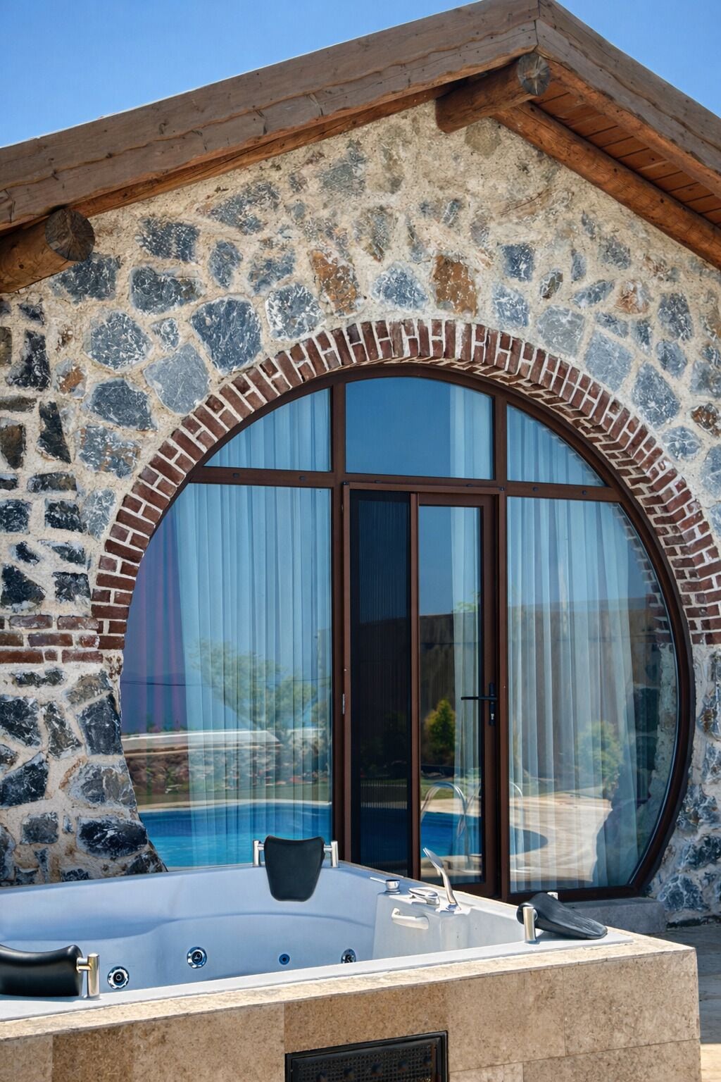 A stone building with a large arched window, a hot tub, and a pool.
