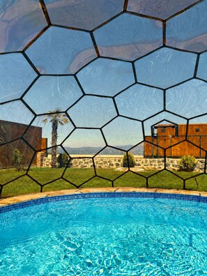 A swimming pool with a hexagonal glass enclosure, surrounded by a grassy area and a wooden fence. - Liva Villa (İznik)