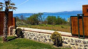 Un jardin avec un mur en pierre, une clôture en bois, un palmier et une vue sur l’océan.