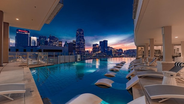 Una piscina en la azotea con sillas de descanso y vista al horizonte de la ciudad al atardecer.