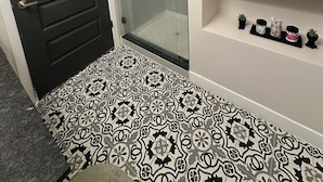 Un baño con ducha, una puerta negra y baldosas de suelo con diseño.
