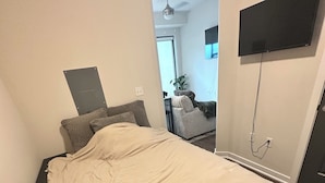 Un dormitorio con una cama, un televisor montado en la pared y una puerta que da a otra habitación.