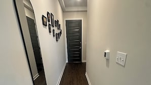 Un pasillo con piso de madera, una puerta al final y un espejo instalado en la pared.