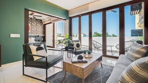 A modern living room with a sofa, armchair, coffee table, and large windows offering a view of the outdoors. - Zona Romantica Condo | Rooftop Pool | 1 Min Beach (Puerto Vallarta)