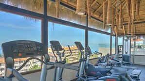 A gym with cardio machines, a weight bench, and a view of the city. - Zona Romantica Condo | Rooftop Pool | 1 Min Beach (Puerto Vallarta)