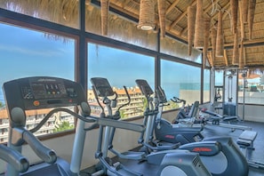 A gym with cardio machines, a weight bench, and a view of the city. - Zona Romantica Condo | Rooftop Pool | 1 Min Beach (Puerto Vallarta)
