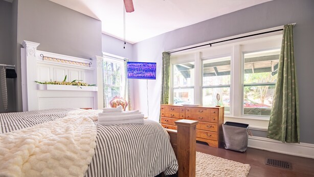 Ein Schlafzimmer mit Bett, Kommode, Fenster und Fernseher.