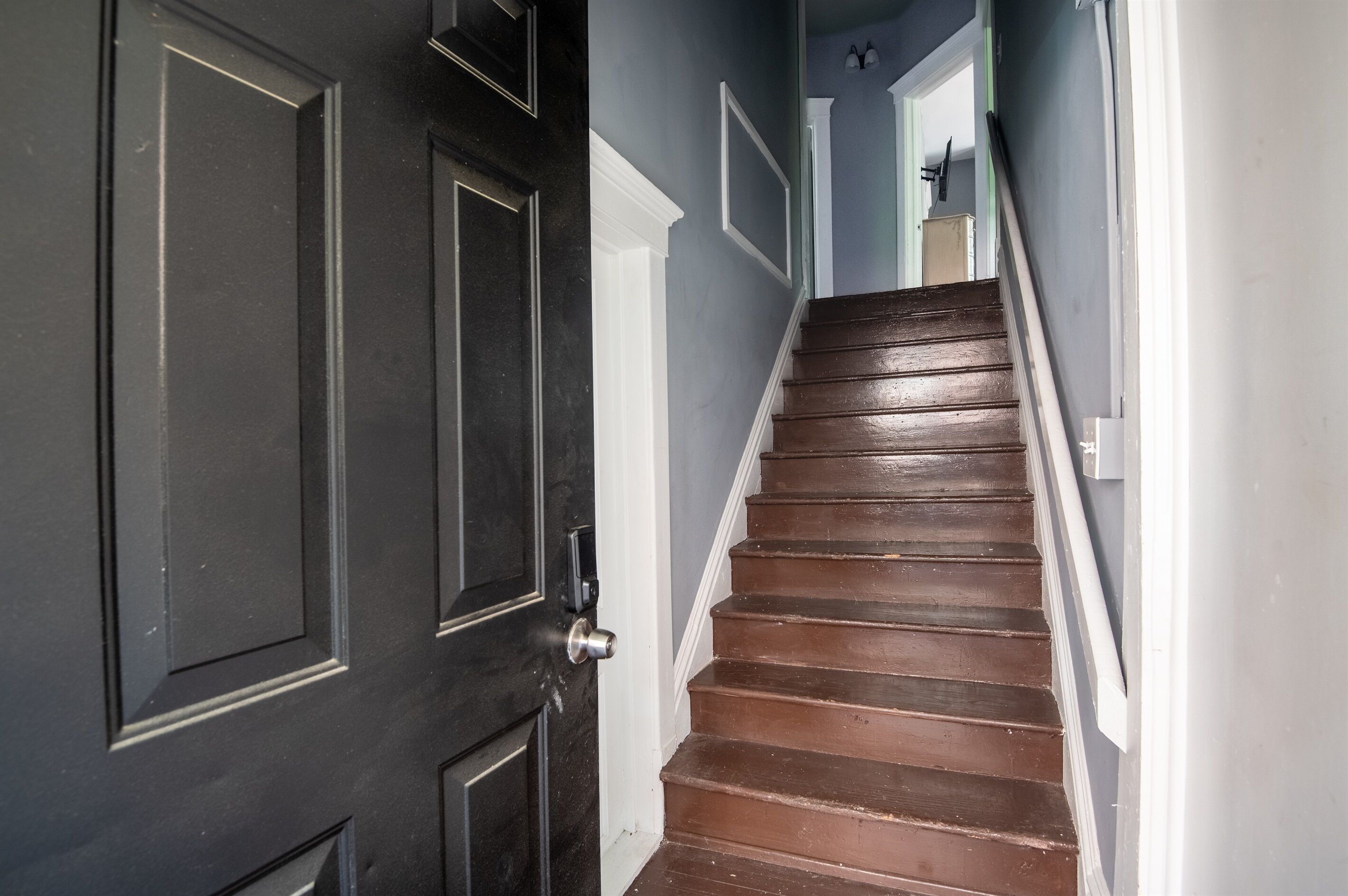 A staircase with dark wooden steps and white trim, leading to a door with a silver handle.
