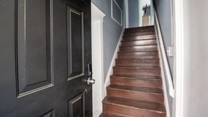 Un escalier avec des marches en bois foncé et des moulures blanches, menant à une porte dotée d’une poignée argentée.