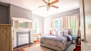 Une chambre à coucher comprenant un lit, un ventilateur de plafond, une cheminée, une commode et une fenêtre avec des rideaux.