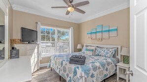 A bedroom with a bed, a ceiling fan, a TV, and a window with a view of trees and a building. - Sleeps 16-inside OL w/ Limo Golf Cart &Game Room (Myrtle Beach)