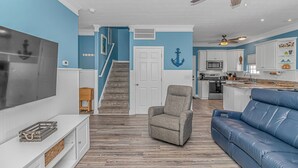 A living room with a TV, a blue couch, a grey armchair, and a staircase leading to a kitchen. - Sleeps 16-inside OL w/ Limo Golf Cart &Game Room (Myrtle Beach)