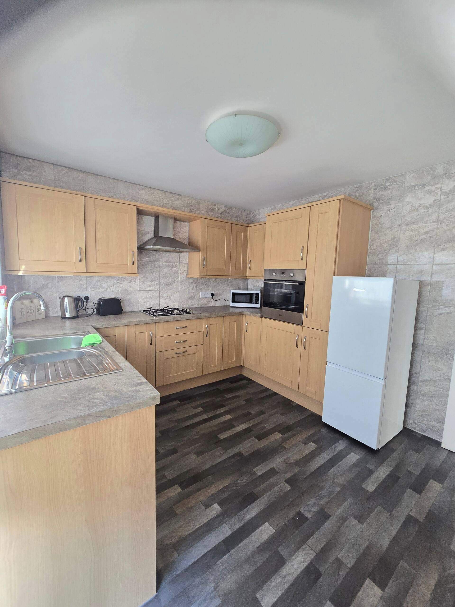 A compact kitchen with wooden cabinets, a gas stove, a microwave, an oven, and a white refrigerator.
