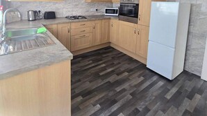 Cocina compacta con armarios de madera, estufa a gas, microondas, horno y refrigerador blanco.