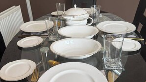 Une table à manger dressée avec des assiettes, des verres, des couverts et une théière, entourée de chaises.