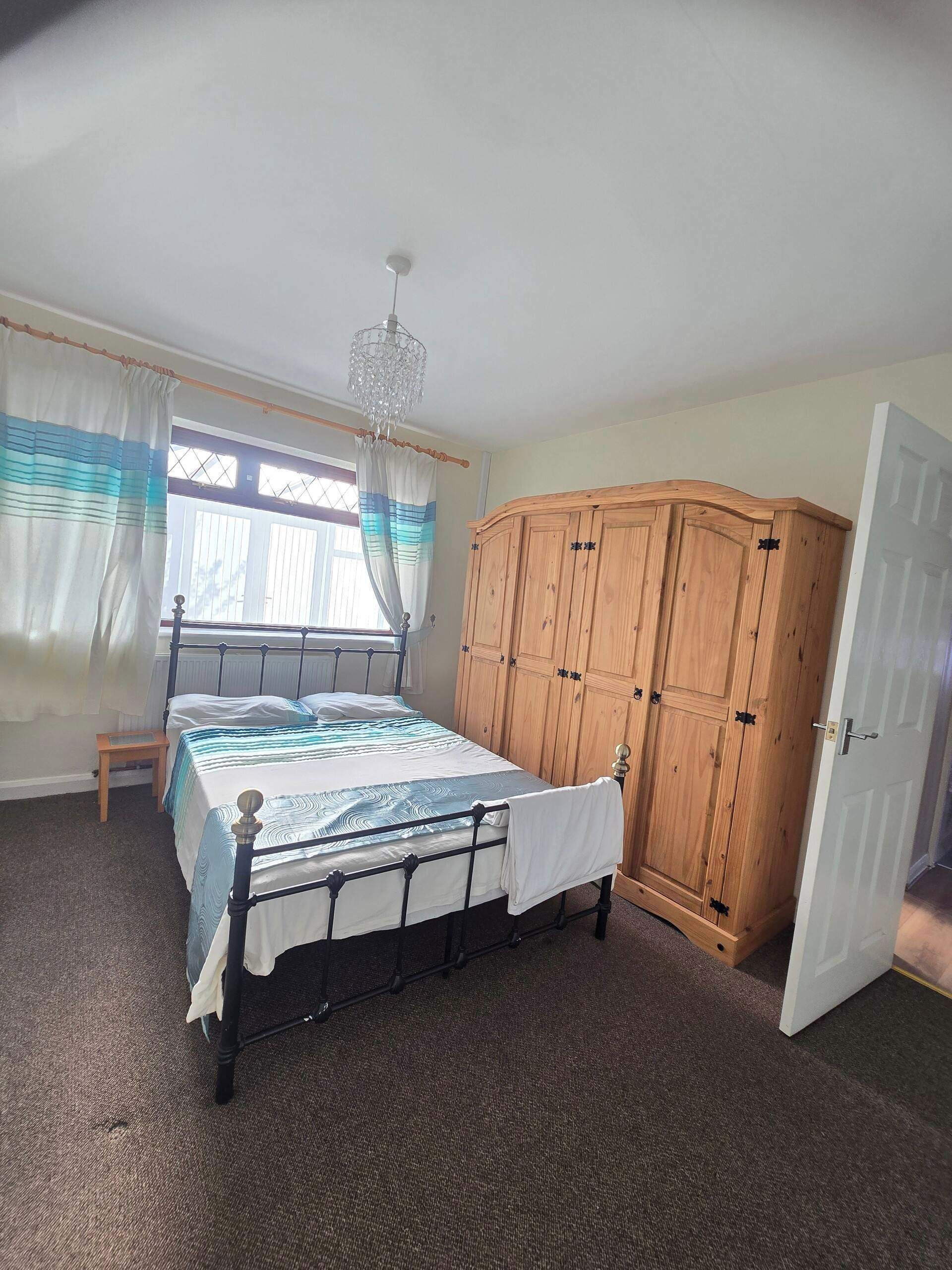 A bedroom with a bed, wooden wardrobe, and a window with curtains.