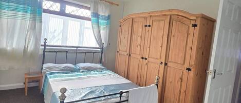 A bedroom with a bed, wooden wardrobe, and a window with curtains.