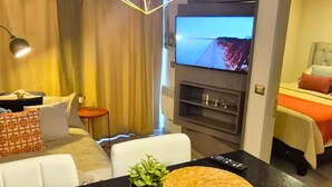 Ett hotellrum med en soffa, ett matbord med en fjärrkontroll, en tv och en säng med ett rött täcke.
