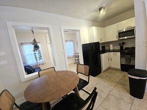 A compact kitchen with white cabinets, a black refrigerator, and a microwave. There is a dining table with chairs, and a trash bin is visible. - Stylish Modern Studio/Private/Close to everything in Fort Lauderdale (Fort Lauderdale)