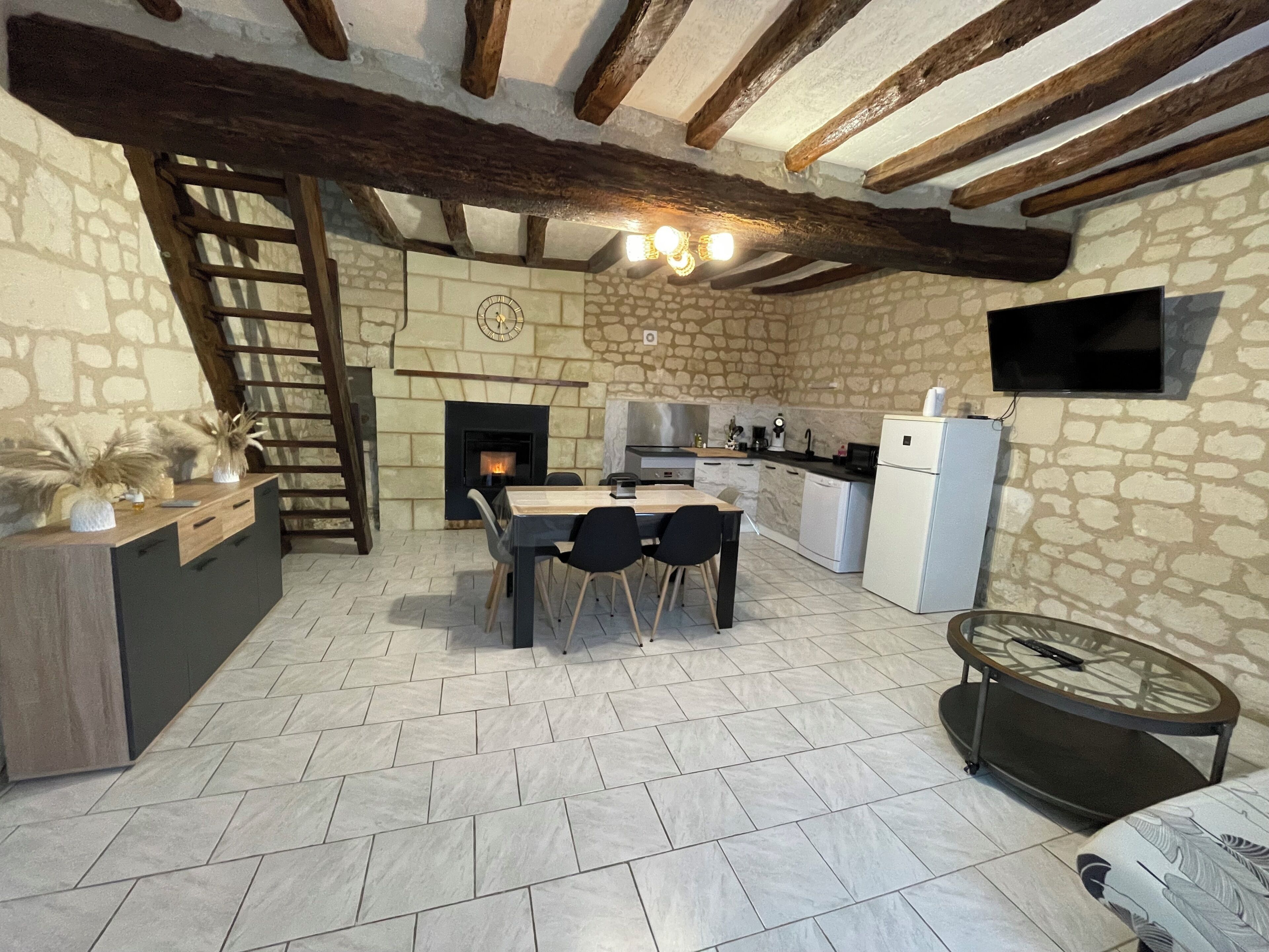 Une cuisine rustique avec des murs en pierre, une cheminée, un plafond en bois et un coin repas comprenant des chaises et une table.