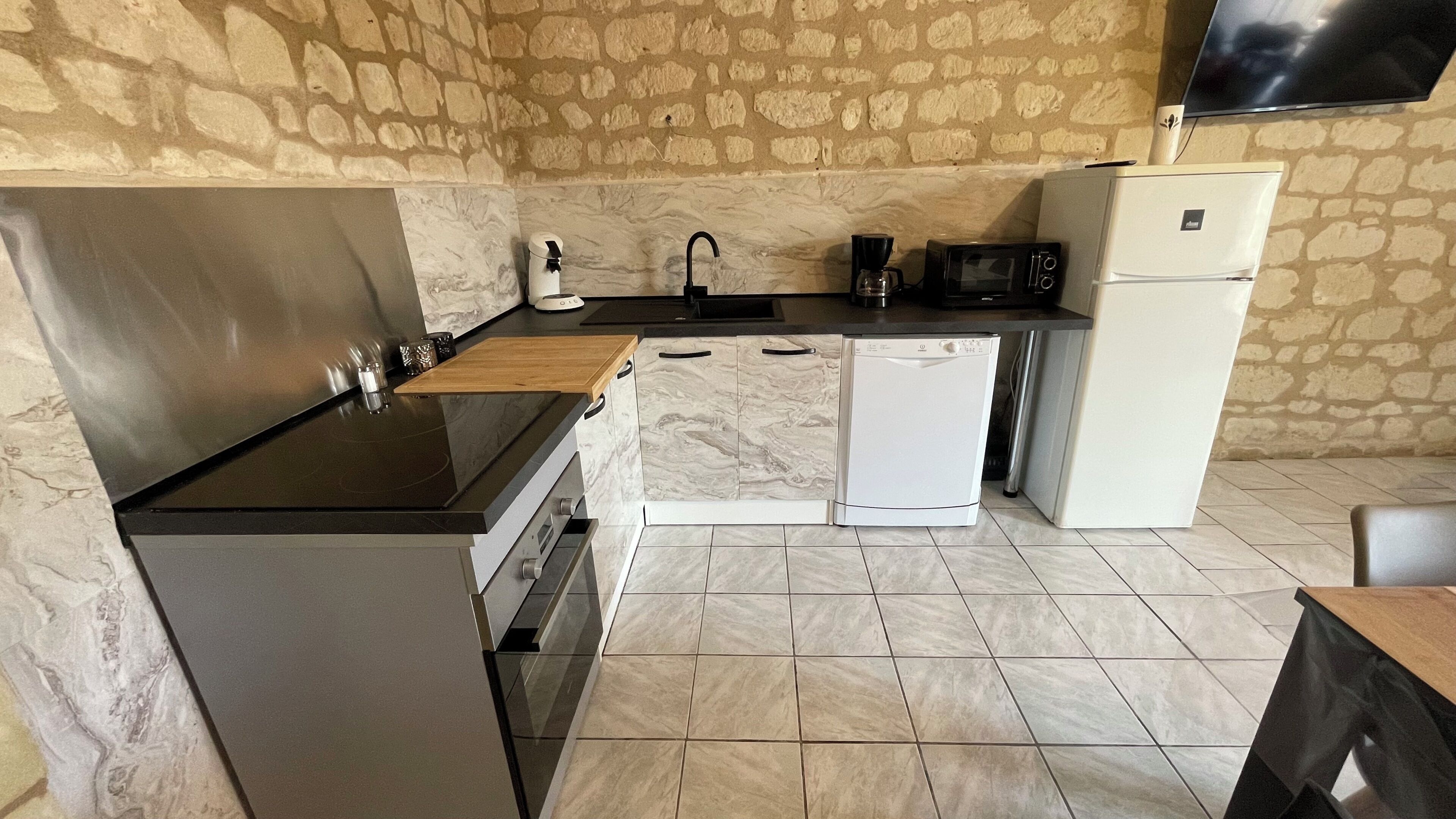 A compact kitchen with a stone wall, a built-in oven, a microwave, a coffee maker, and a refrigerator.