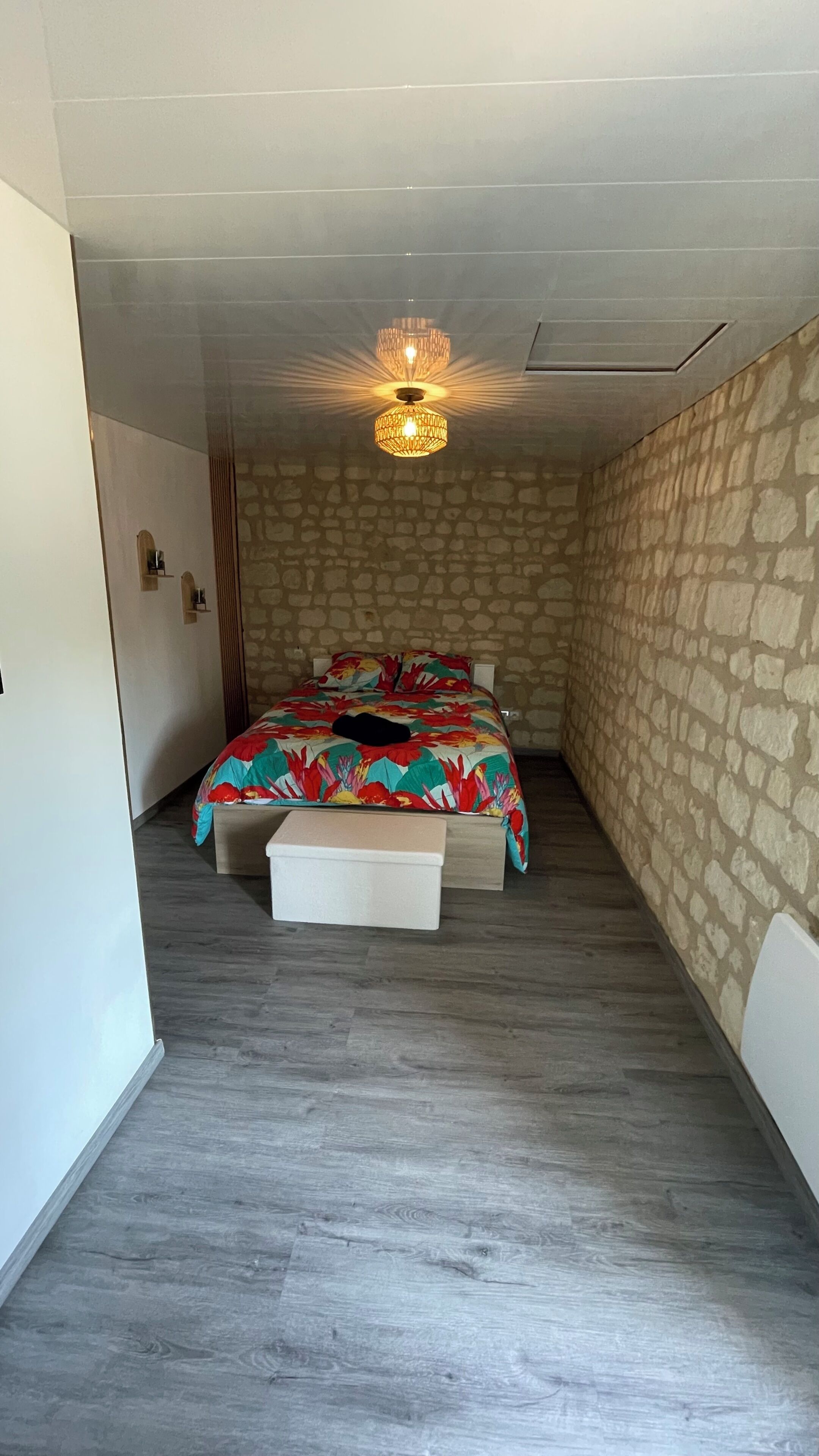 Une chambre à coucher avec un lit, un banc, un mur en pierre et un luminaire au plafond.