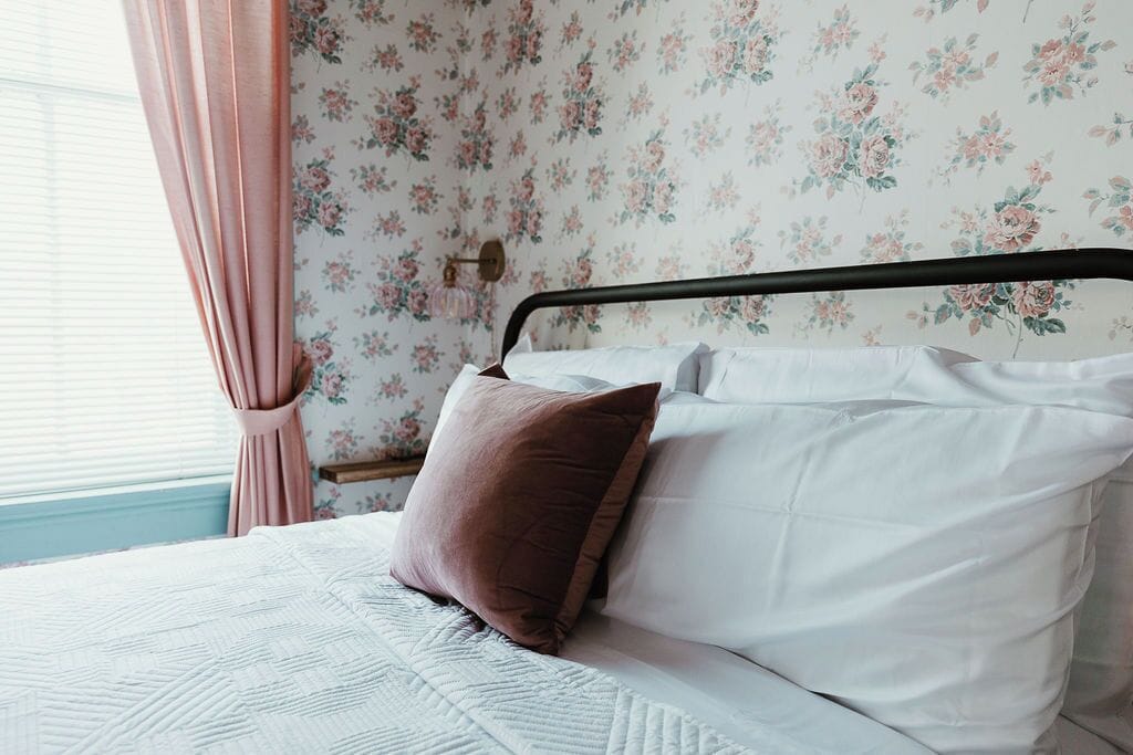 Cama com estrutura de metal, roupa de cama branca e travesseiro marrom.