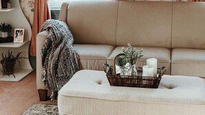 Una sala de estar acogedora con un sofá, una mesita auxiliar, un cesto con adornos y una ventana con cortinas.