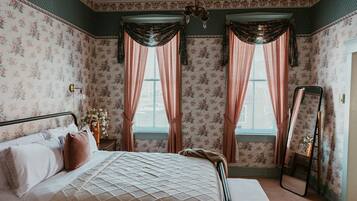 Una camera da letto con un letto, carta da parati floreale, tende, uno specchio e un lampadario.