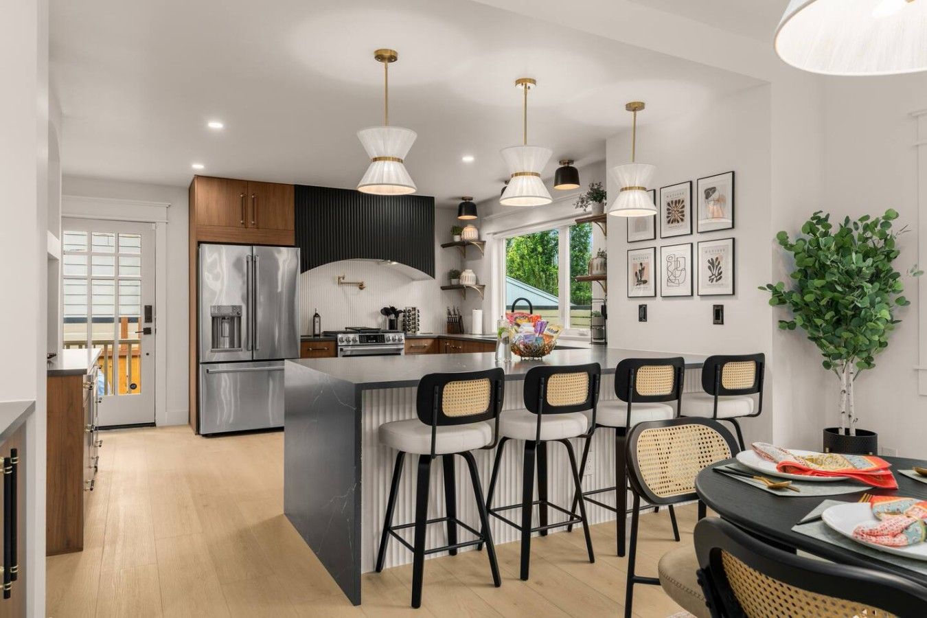 A modern kitchen with a central island, bar stools, pendant lighting, and a dining area with a table and chairs.