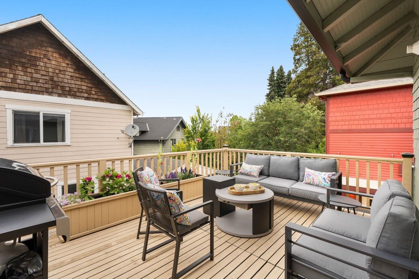 A deck with outdoor furniture, a barbecue grill, and a red building in the background.