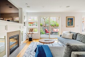 A modern living room with a fireplace, a sofa, a coffee table, and a view of the backyard through large sliding glass doors. - Dreamy SandPoint Retreat | 3 BDRMs, Near Hospitals (Seattle)