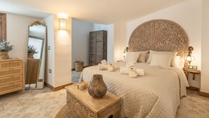 Ein Schlafzimmer mit einem großen Bett, Nachttischlampen, einem Spiegel, einem Schminktisch und einem kleinen Tisch mit einer Vase.