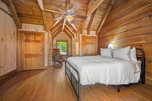 A bedroom with a bed, wooden walls, a ceiling fan, and a window. - Starling Road Retreat - Cabin with Stunning Views (Lake Lure)