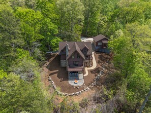 A two-story house with a stone foundation, a wrap-around porch, and a stone retaining wall. - Starling Road Retreat - Cabin with Stunning Views (Lake Lure)