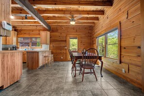 A wooden cabin interior with a kitchen, dining area, and large windows. - Starling Road Retreat - Cabin with Stunning Views (Lake Lure)