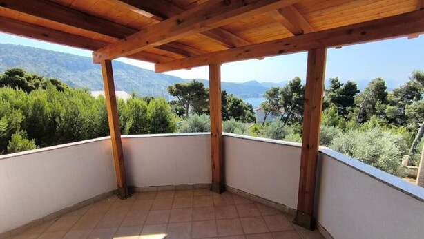 Uma área externa coberta com piso de azulejos, vigas de madeira e vista para vegetação e montanhas.