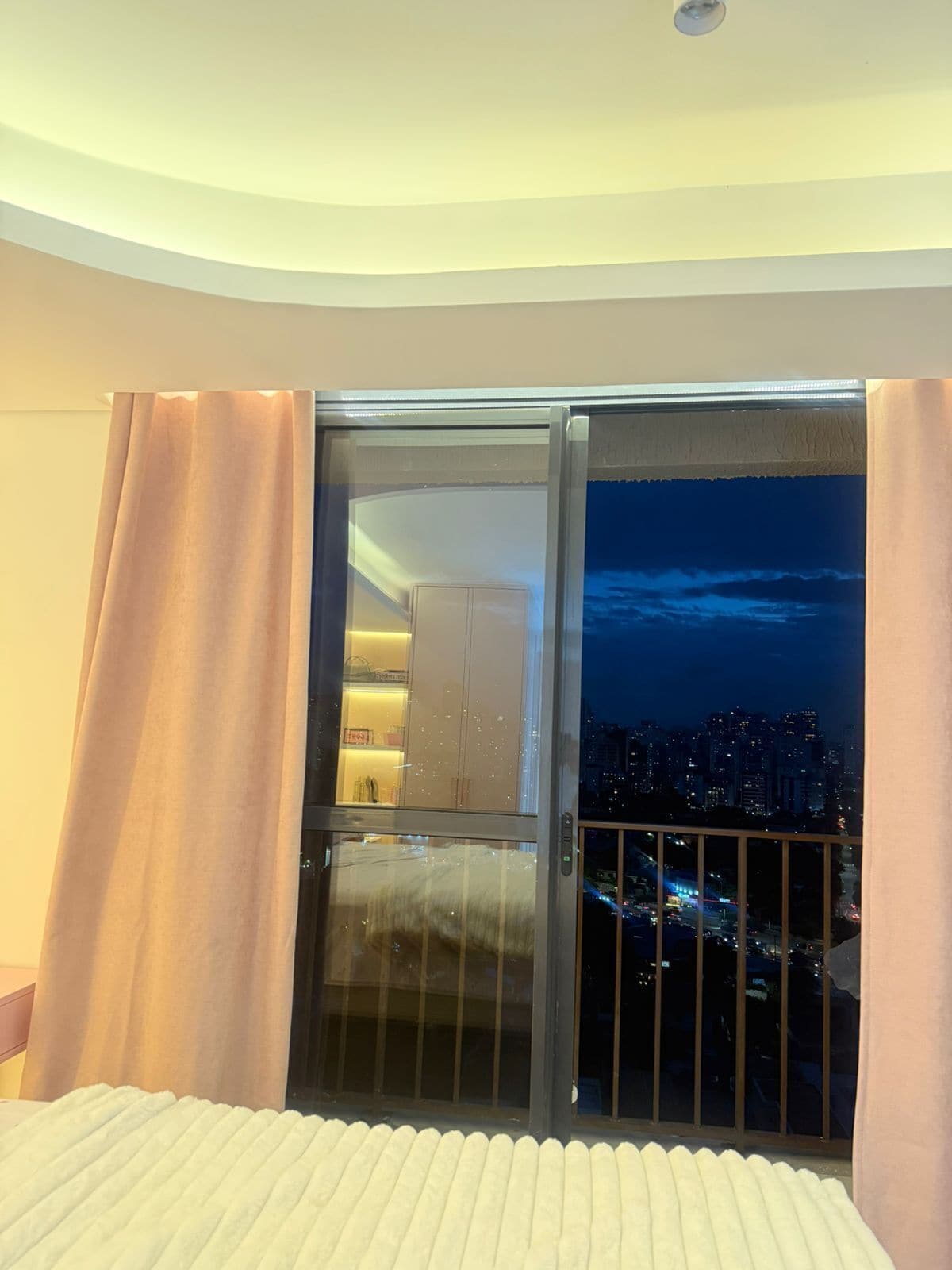 A hotel room with a sliding glass door leading to a balcony with a city view at night.