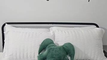Ein Bett mit weißer Bettwäsche, ein grünes Kissen und eine Wand mit dem Text 'lets stay in bed'.