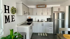 Een moderne keuken met witte kasten, roestvrijstalen apparatuur en een grijze betegelde vloer.