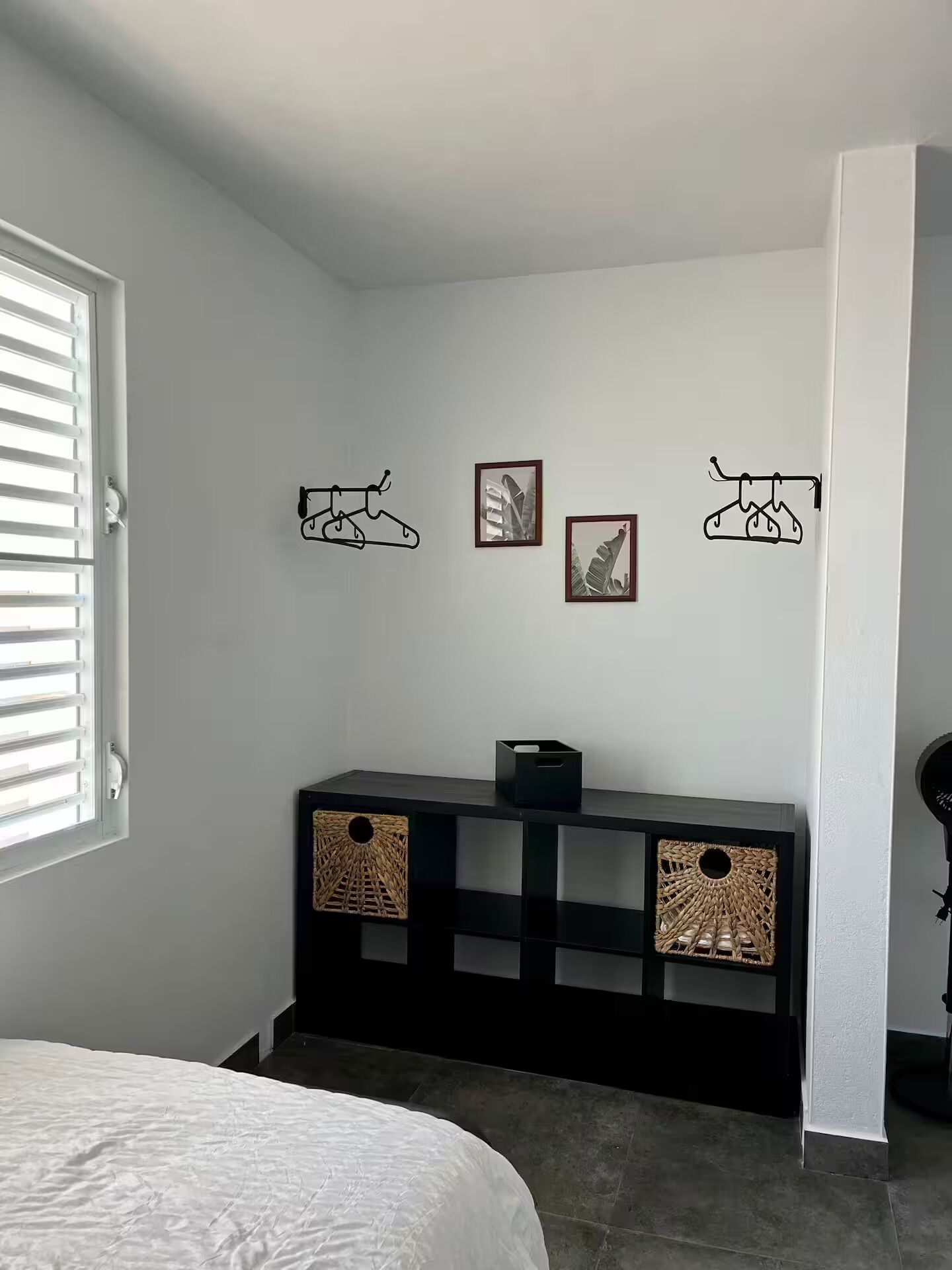 Un dormitorio con cama, una consola negra con cestas tejidas y decoración en la pared.