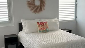 Een slaapkamer met een bed, twee nachtkastjes, een aan de muur bevestigde krans en twee ramen met jaloezieën.