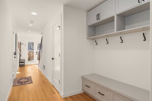 A hallway with a wooden floor, white walls, a bench, and a coat rack. - Dreamy Wallingford Lux Home| 360° Rooftop Deck (Seattle)