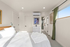 A hotel room with a bed, a bedside table, a wardrobe, a bathroom visible through an open door, and a window with curtains. - Dreamy Wallingford Lux Home| 360° Rooftop Deck (Seattle)