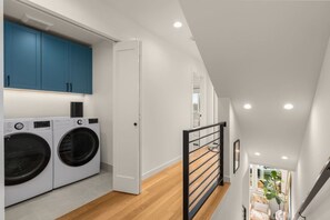 A laundry area with two washing machines, a blue cabinet, and a white door. - Dreamy Wallingford Lux Home| 360° Rooftop Deck (Seattle)